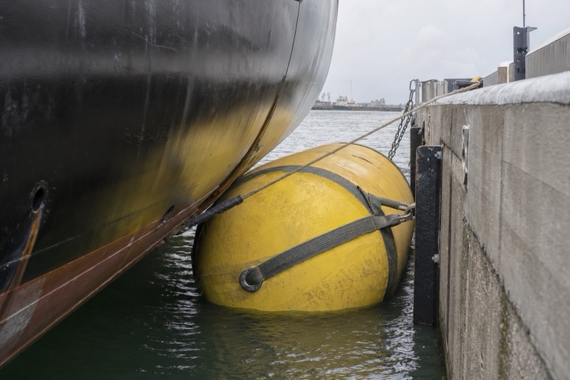 Sling type foam filled fender floating between a ship hull and a quay wall