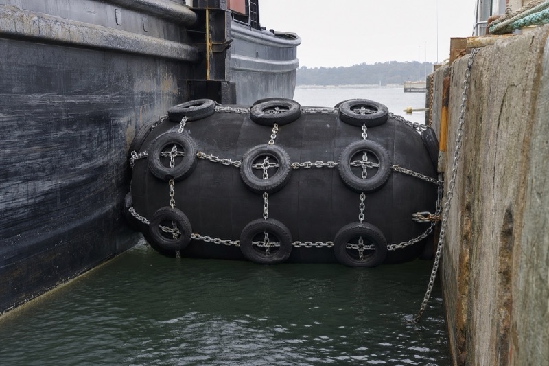 Tire chain net foam filled fender wrapped in a chain-and-tire net between a ship hull and quay