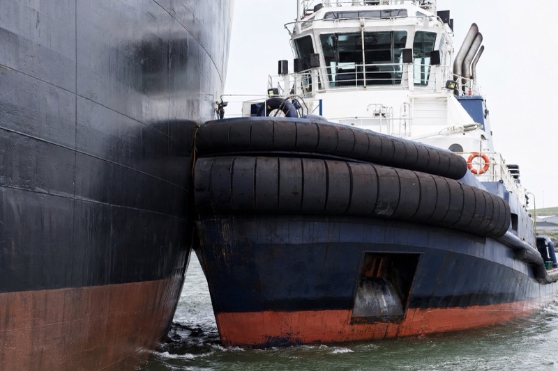 A harbor tug with rubber bow and side fenders pushing against a ship hull